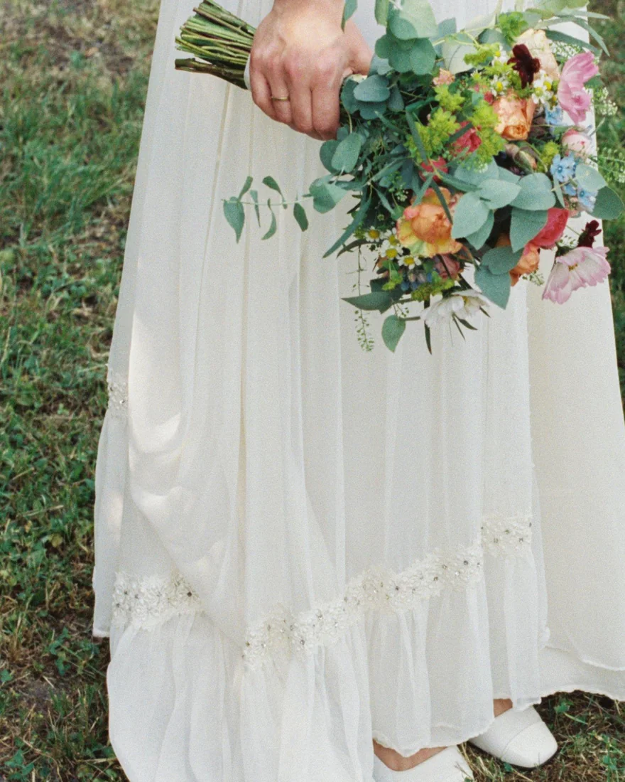 Saum eines hellen Vintage-Brautkleids mit Brautstrauß